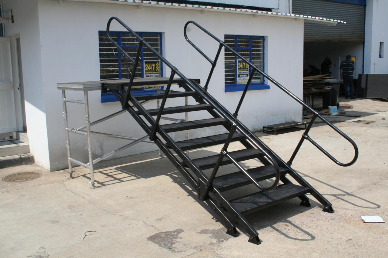 Aluminium hand railing with integrated stairs and safety handrails, designed for event access and crowd control, mounted on a concrete surface.