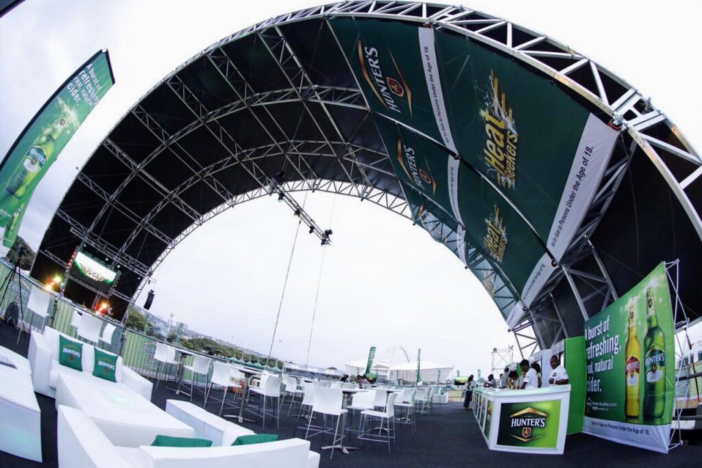 Aluminium trussing arch structure supporting event stage with banners and seating area, designed for engineering and event production applications.