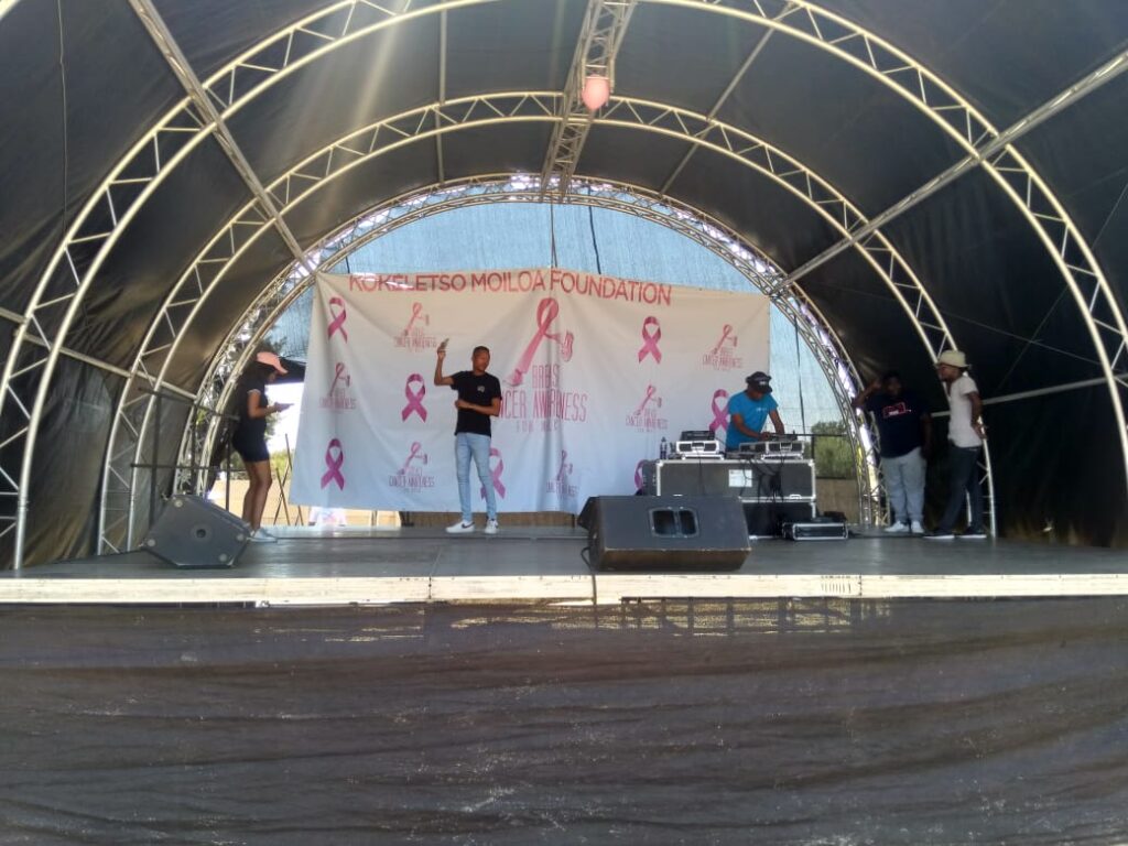 Aluminium trussing structure supporting a stage with a curved roof, used for event production and engineering applications, with performers and DJ set.