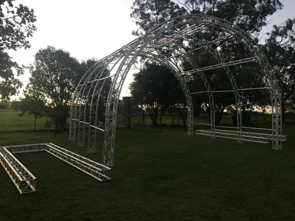 Aluminium trussing arch structure with curved and straight sections, suitable for event staging and rigging in outdoor environments.