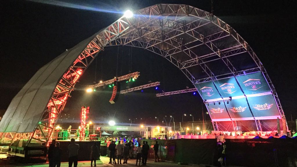 A large aluminium trussing arch structure supporting stage lighting and rigging for an outdoor event at night.