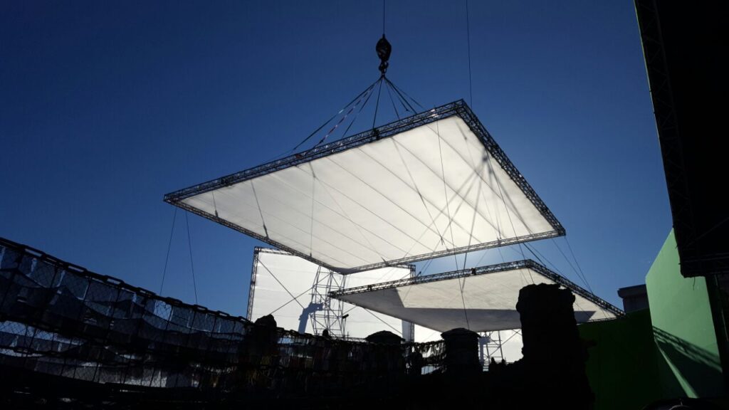Aluminium trussing structure supporting large rectangular LED screens for event production and stage design, with a clear blue sky background.